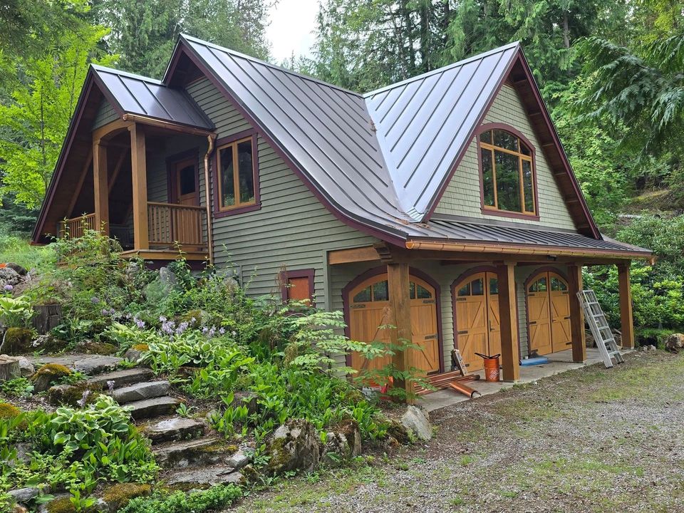 Rustic green house with wood trim and metal roof nestled in a forested hillside.