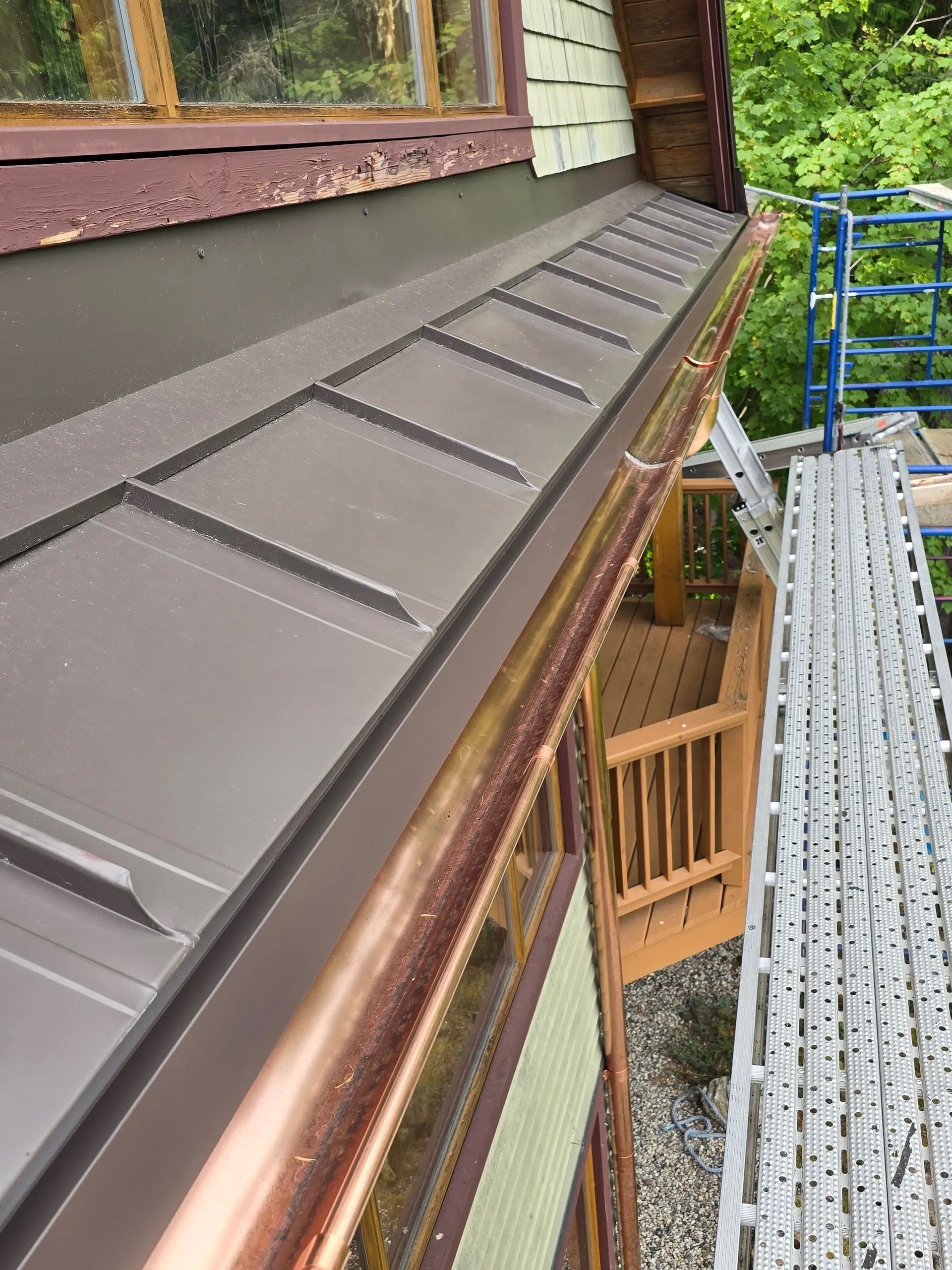Roof edge with brown metal flashing beside a building, viewed from a scaffold walkway