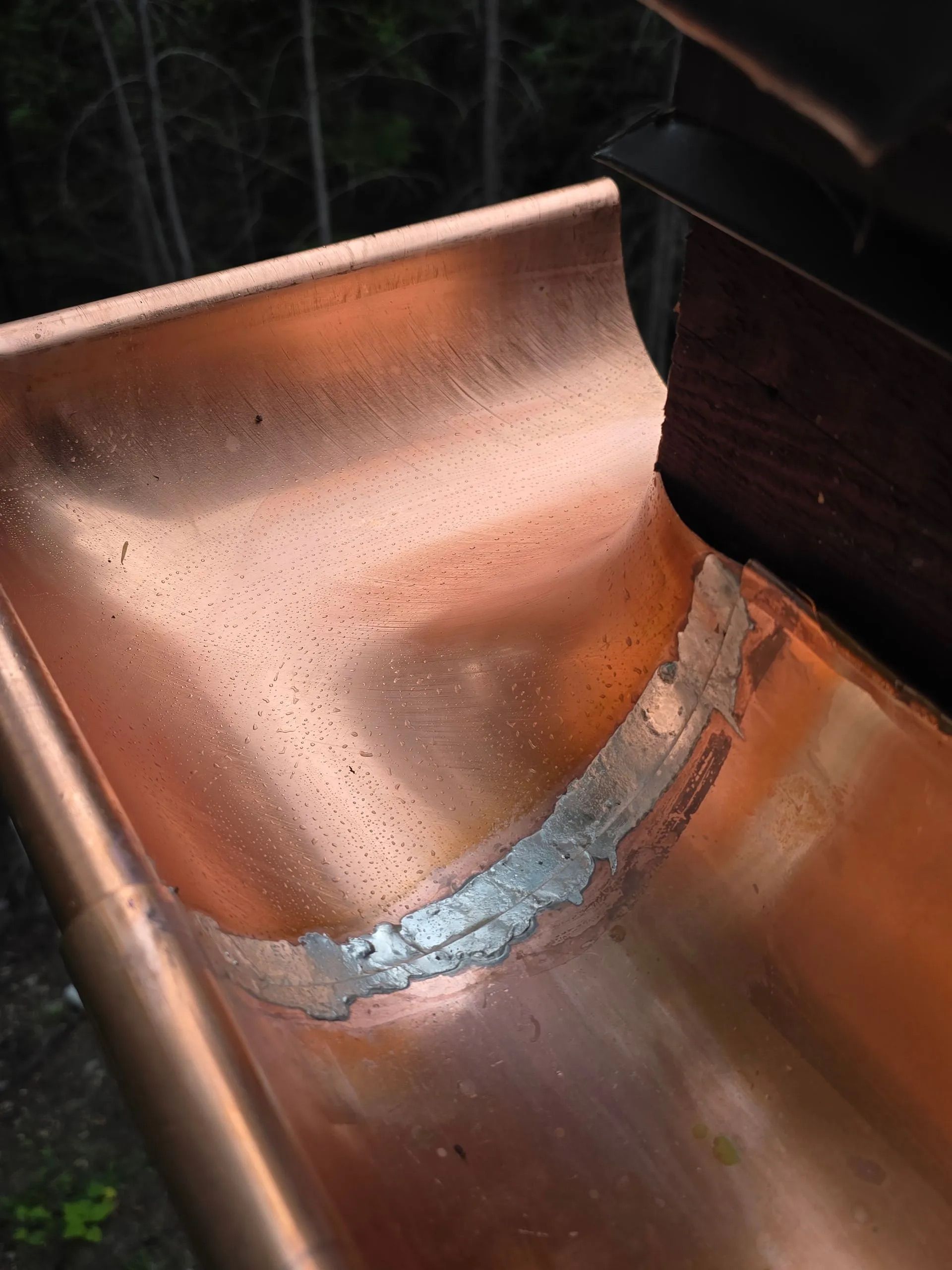 Close-up of a copper gutter seam with visible soldering and water stains