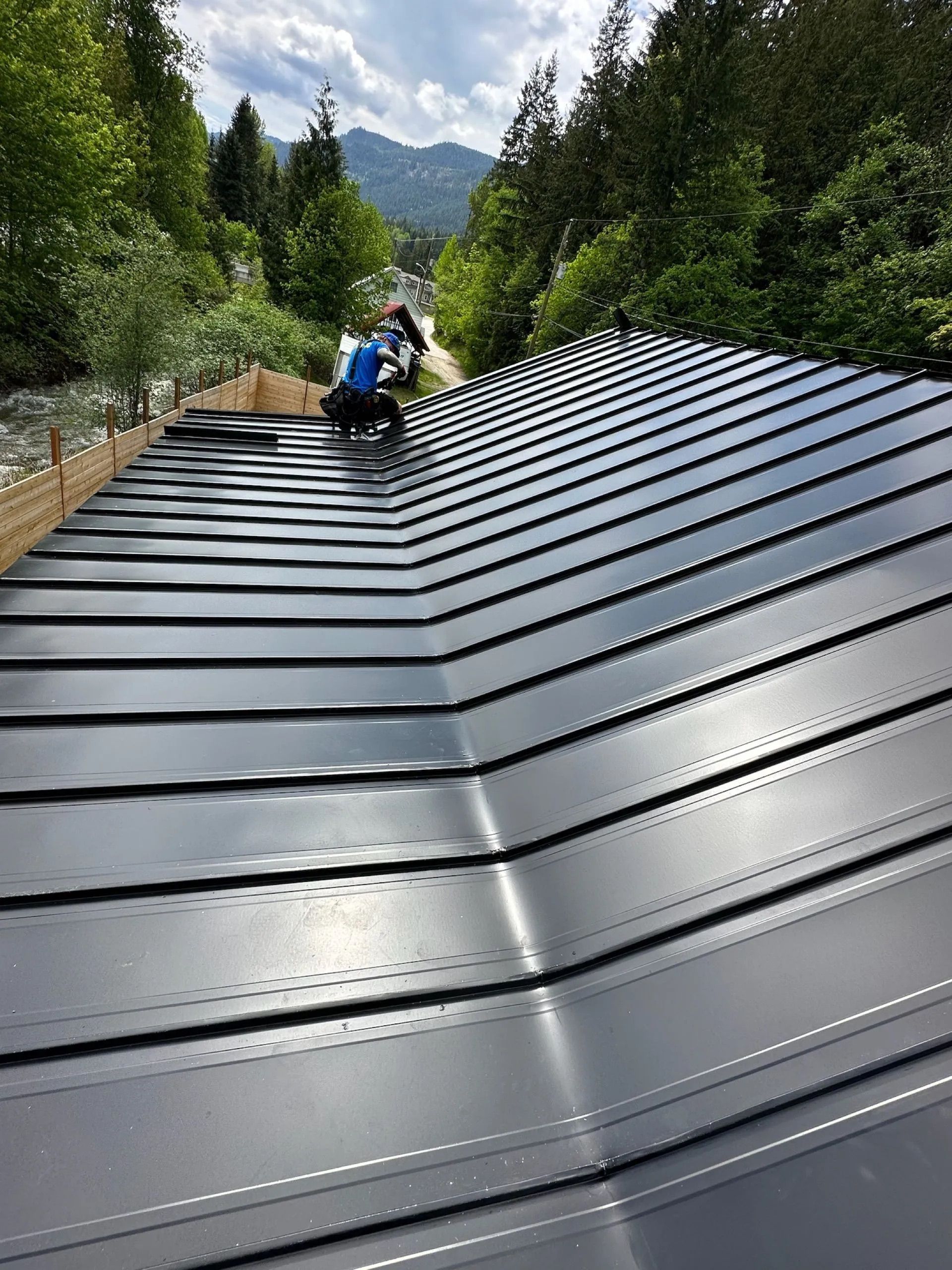 Worker on a steep black metal roof in a wooded mountain area