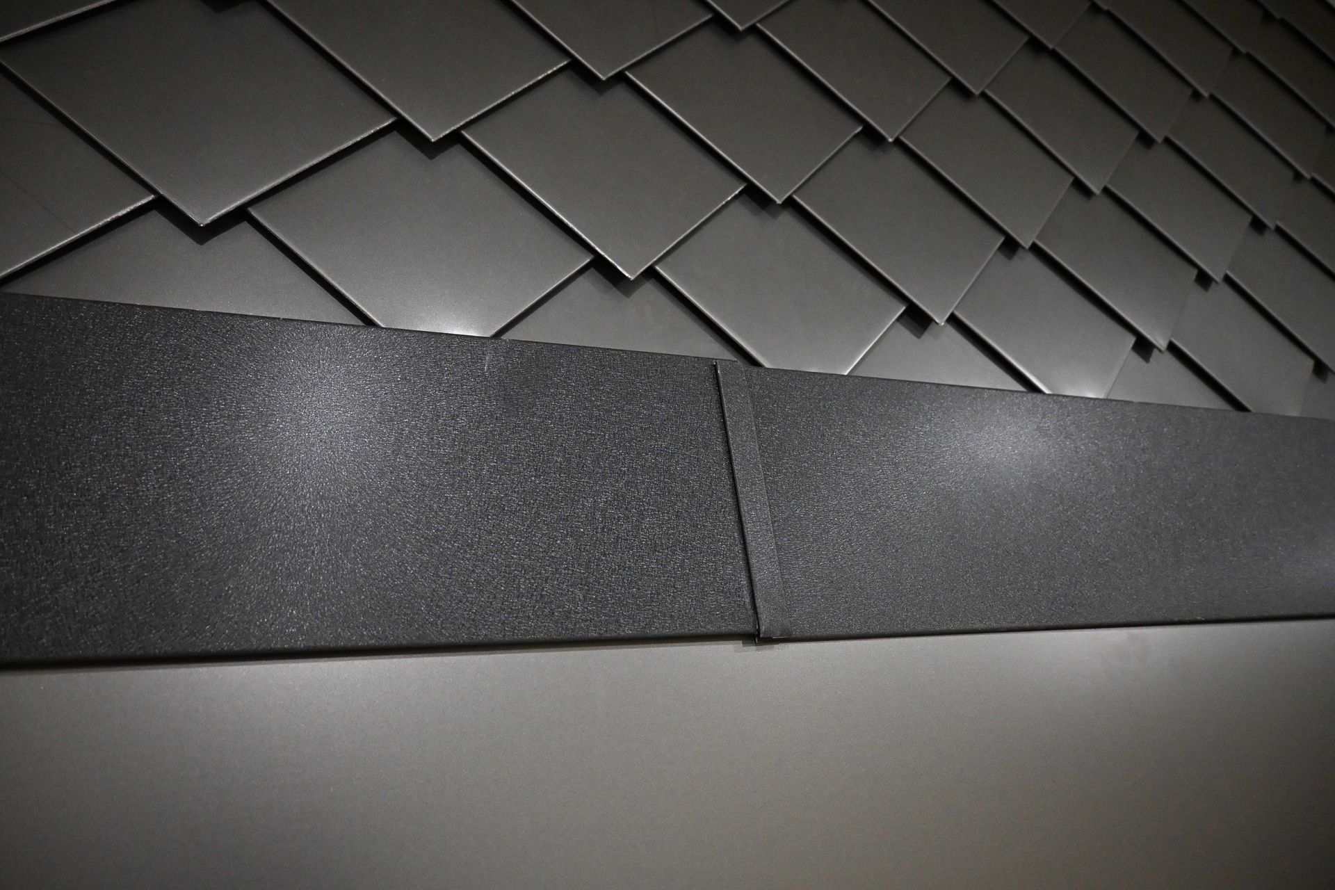 Close-up of dark gray roof shingles with a smooth metal edge in the foreground