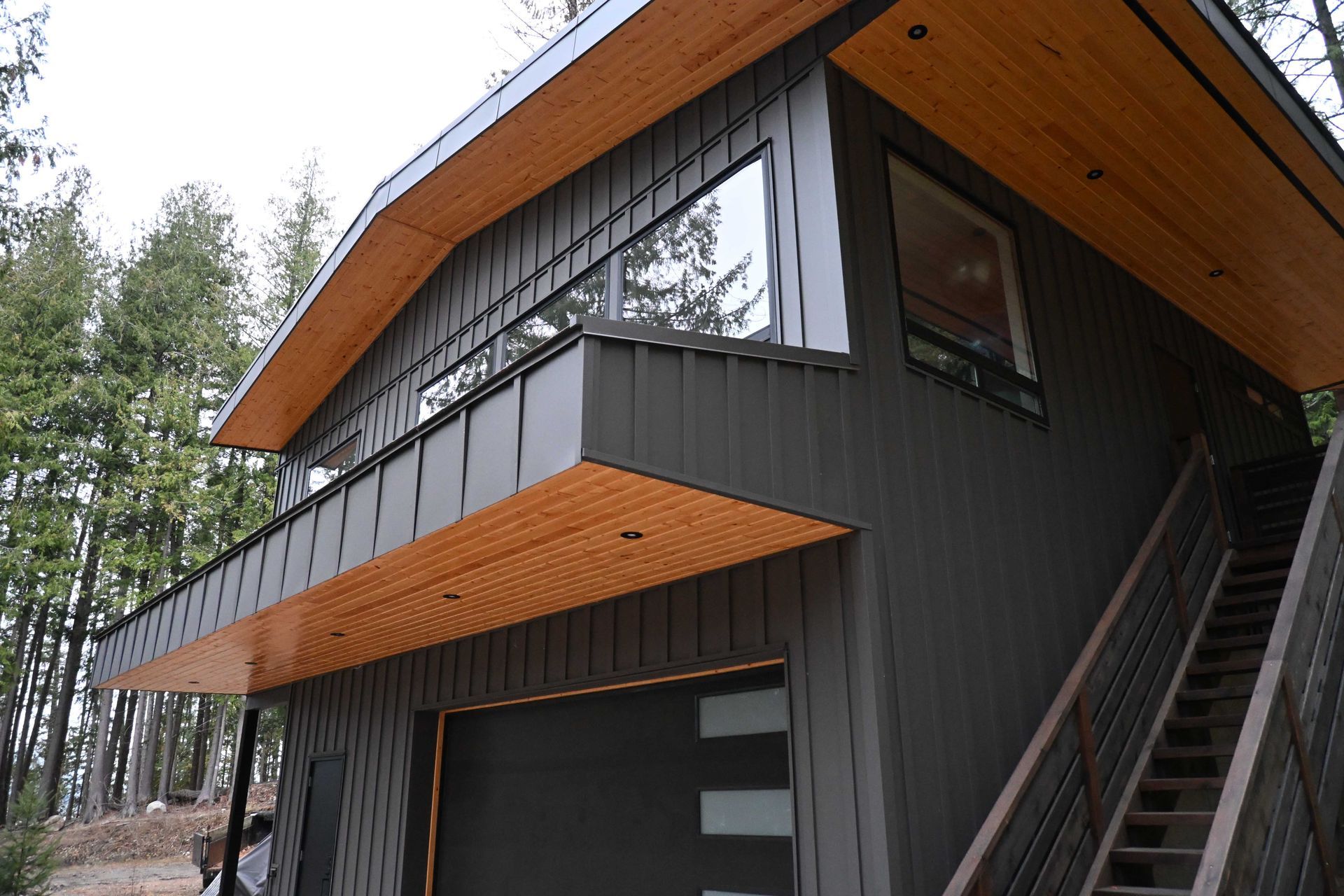 Modern dark-gray house with wood-trimmed overhanging roof in a wooded setting