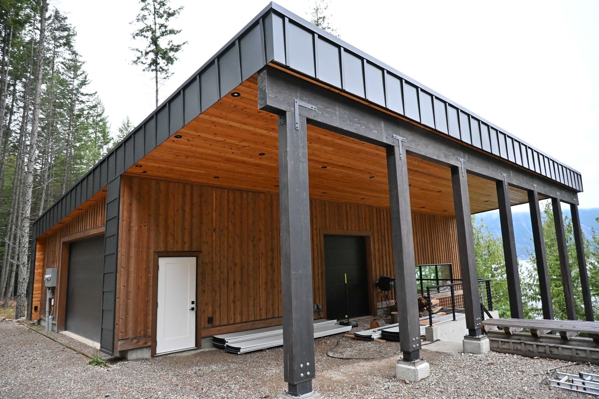 Modern cabin with wood siding, black roof, and large covered porch in a forest setting