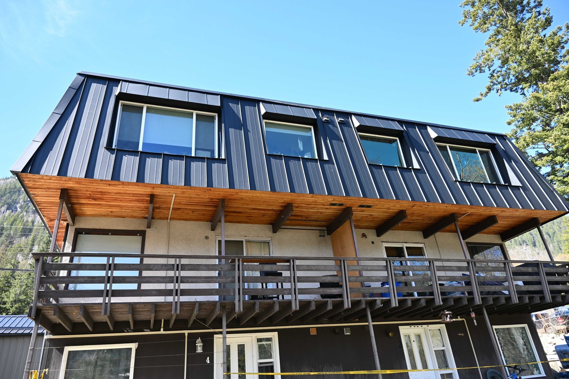 Modern two-story house with black metal roof, wood accents, and a large front balcony under a blue sky