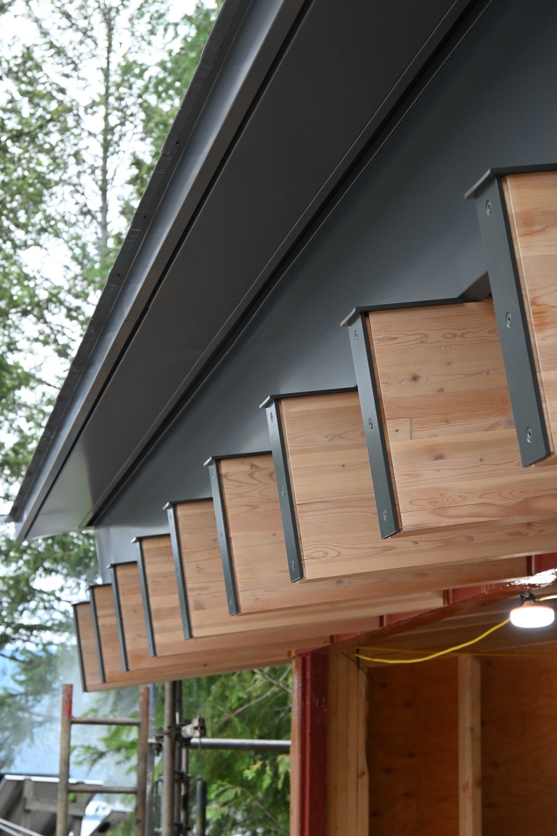Close-up of a house eave with exposed wooden rafters and dark trim under construction