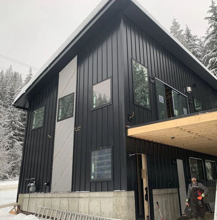 Black modern cabin with large windows and a wood overhang in a snowy setting
