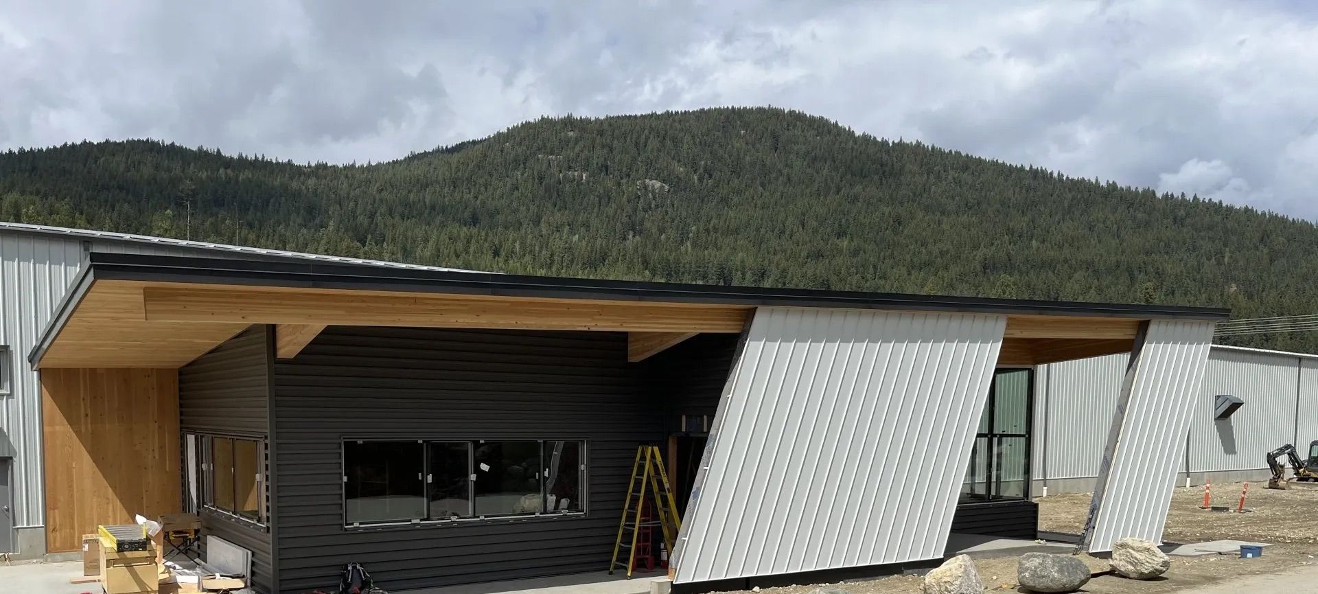 Modern building with a slanted metal facade and wood overhang in a rural mountain setting
