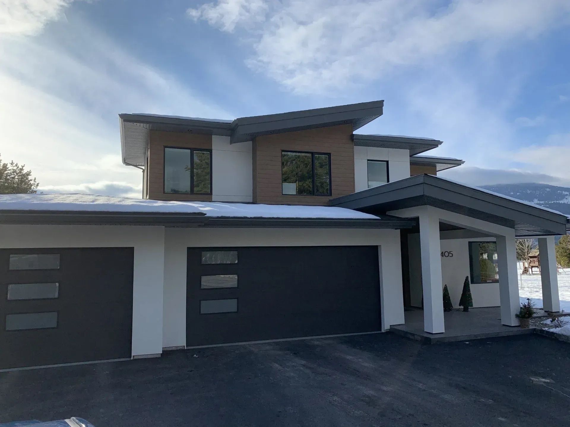 Modern two-story house with a gray facade, dark garage doors, and a covered driveway under a blue sky