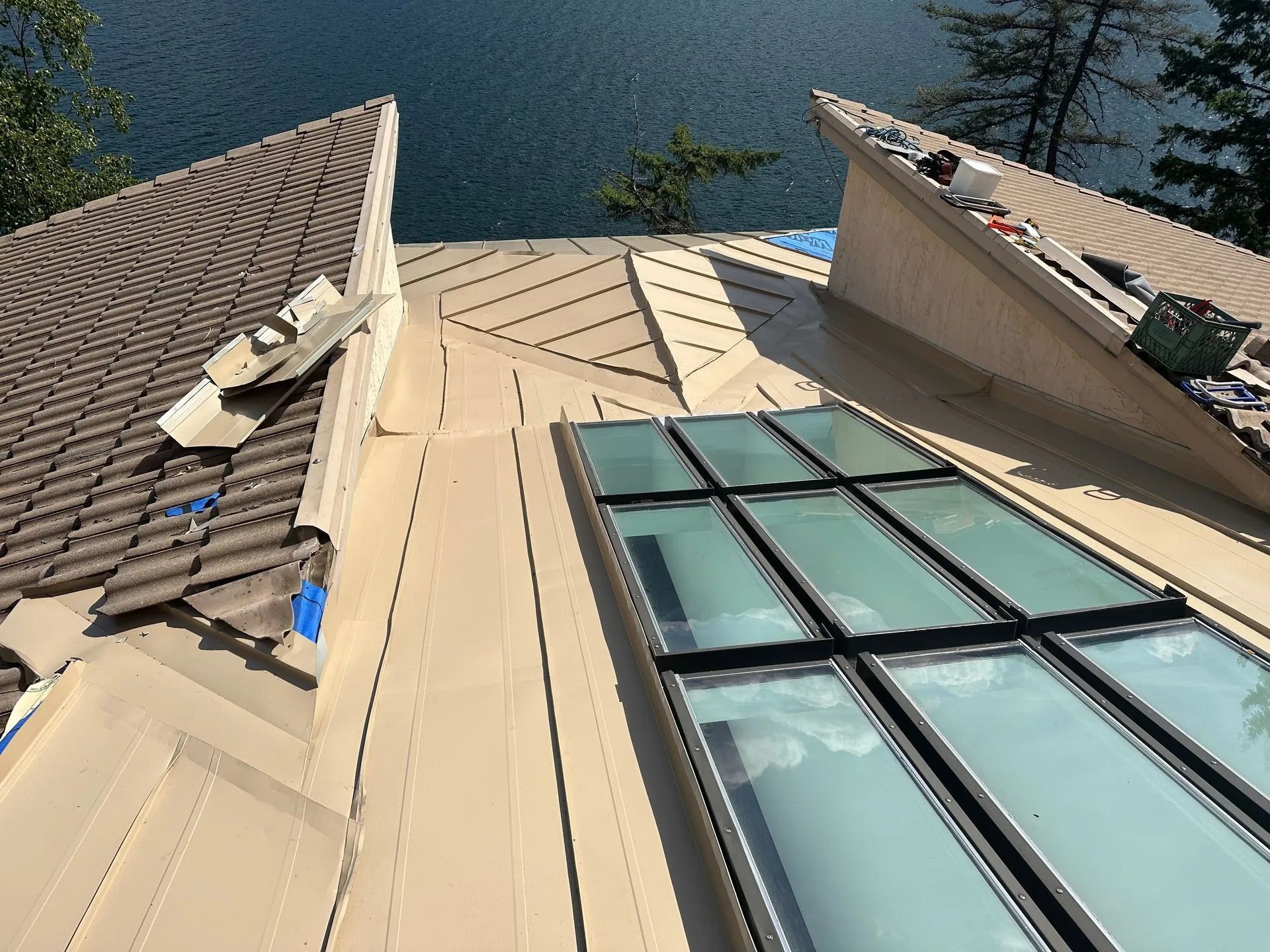 View up from a modern building’s roof beside water, with beige siding and large windows.