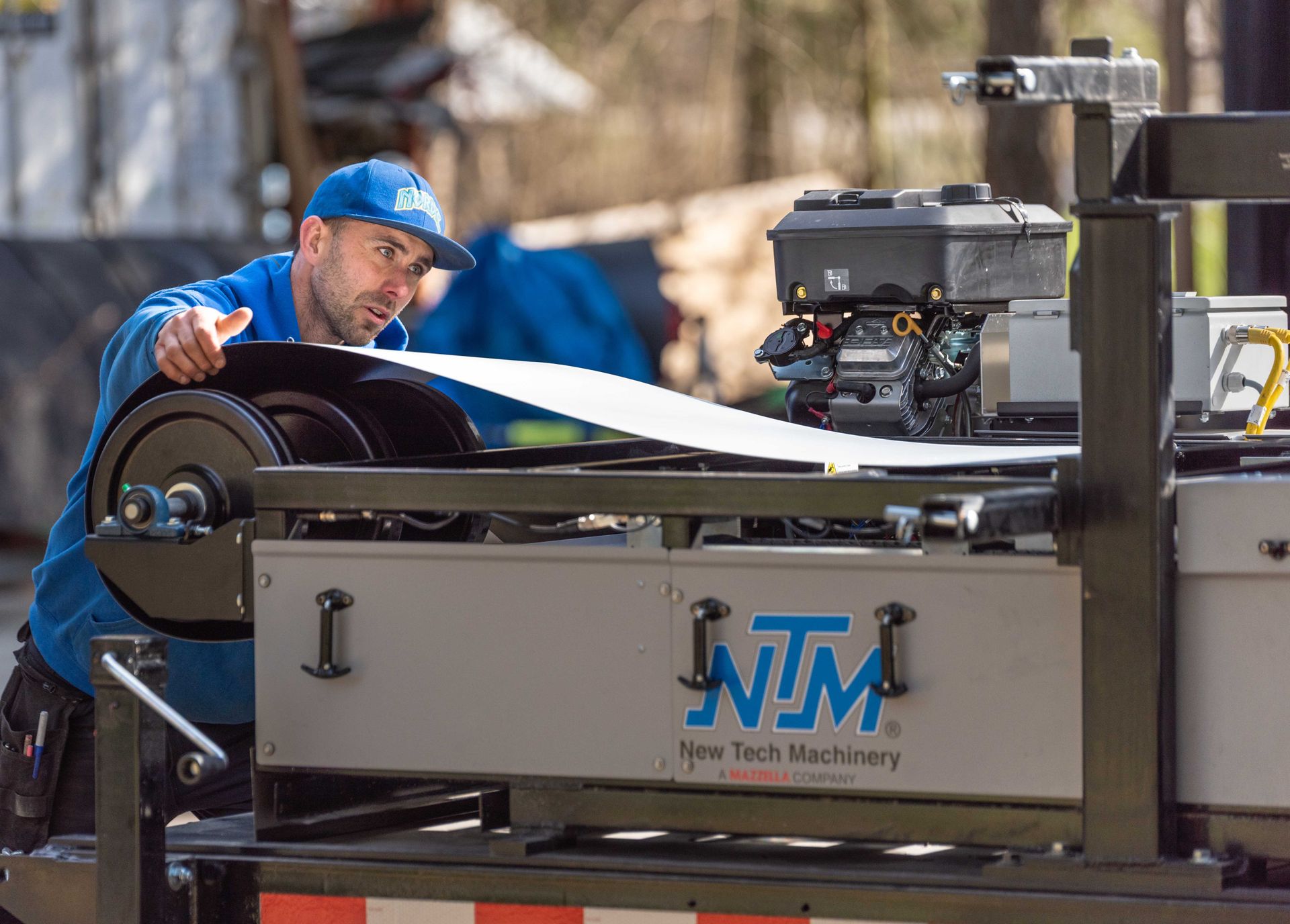 Worker in blue cap operates a machinery conveyor in an industrial workshop