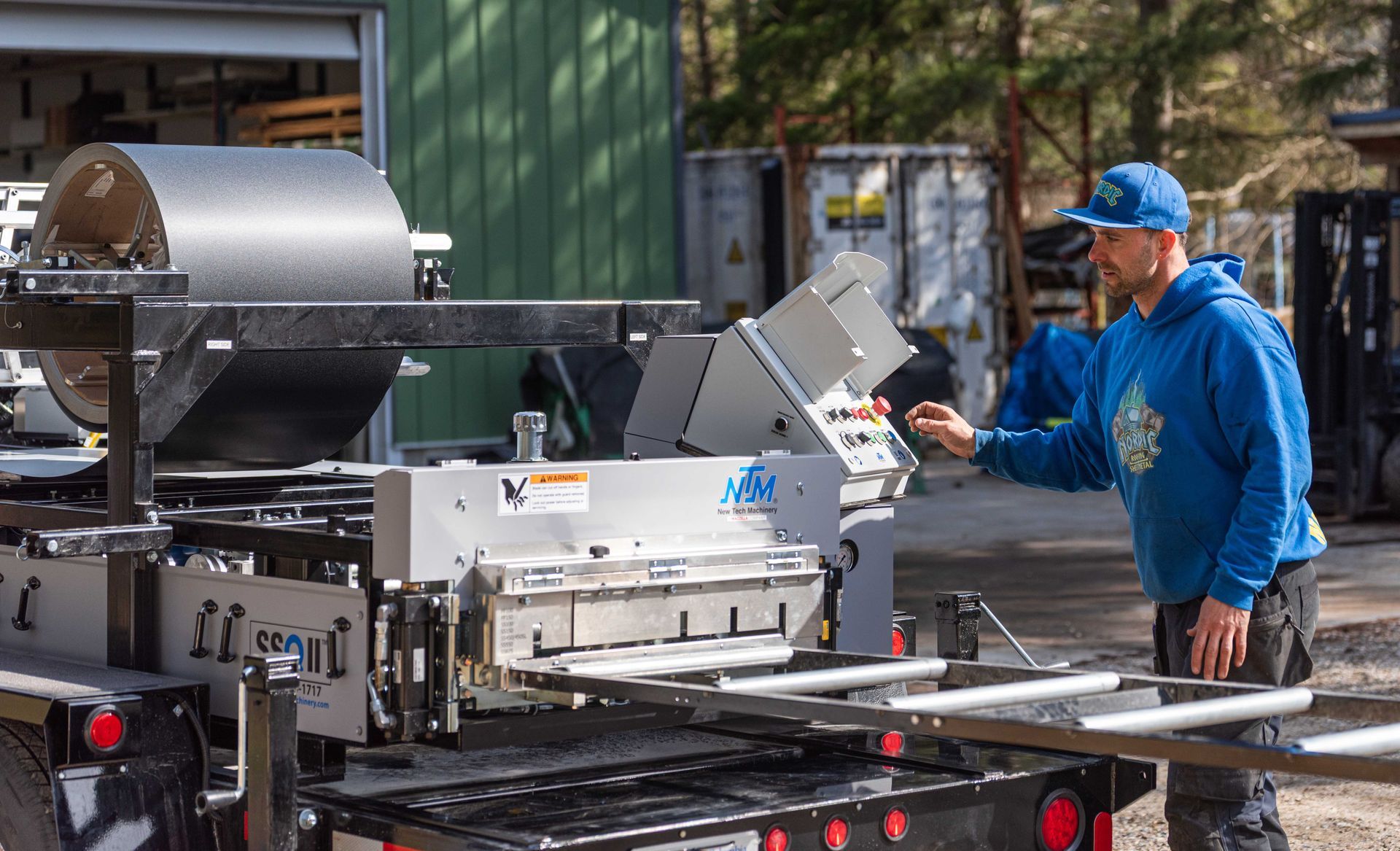 Worker in blue cap and jacket operating industrial machinery outdoors in a factory yard.
