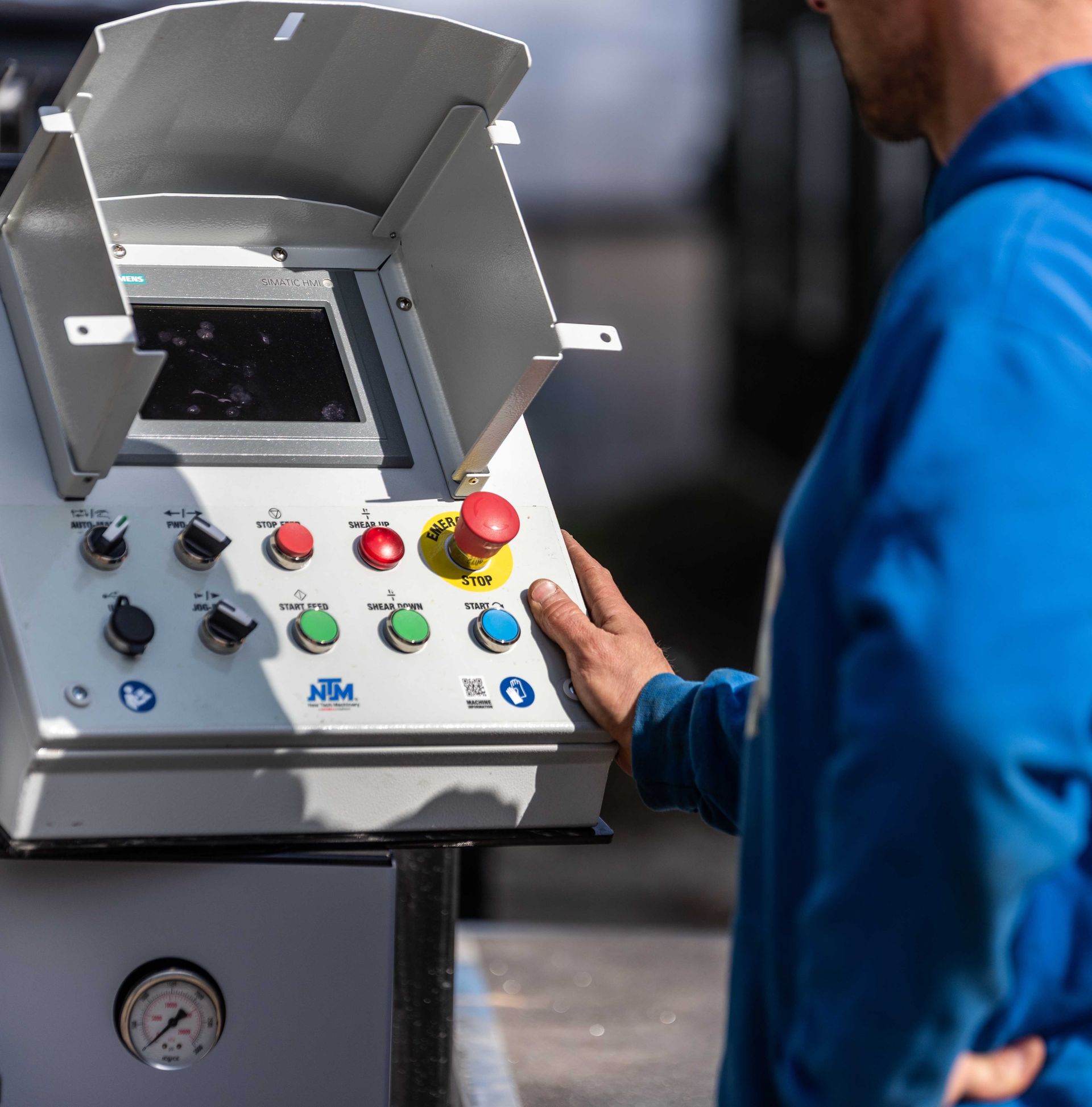 Worker operating a control panel on industrial machinery with colorful buttons and a raised safety cover