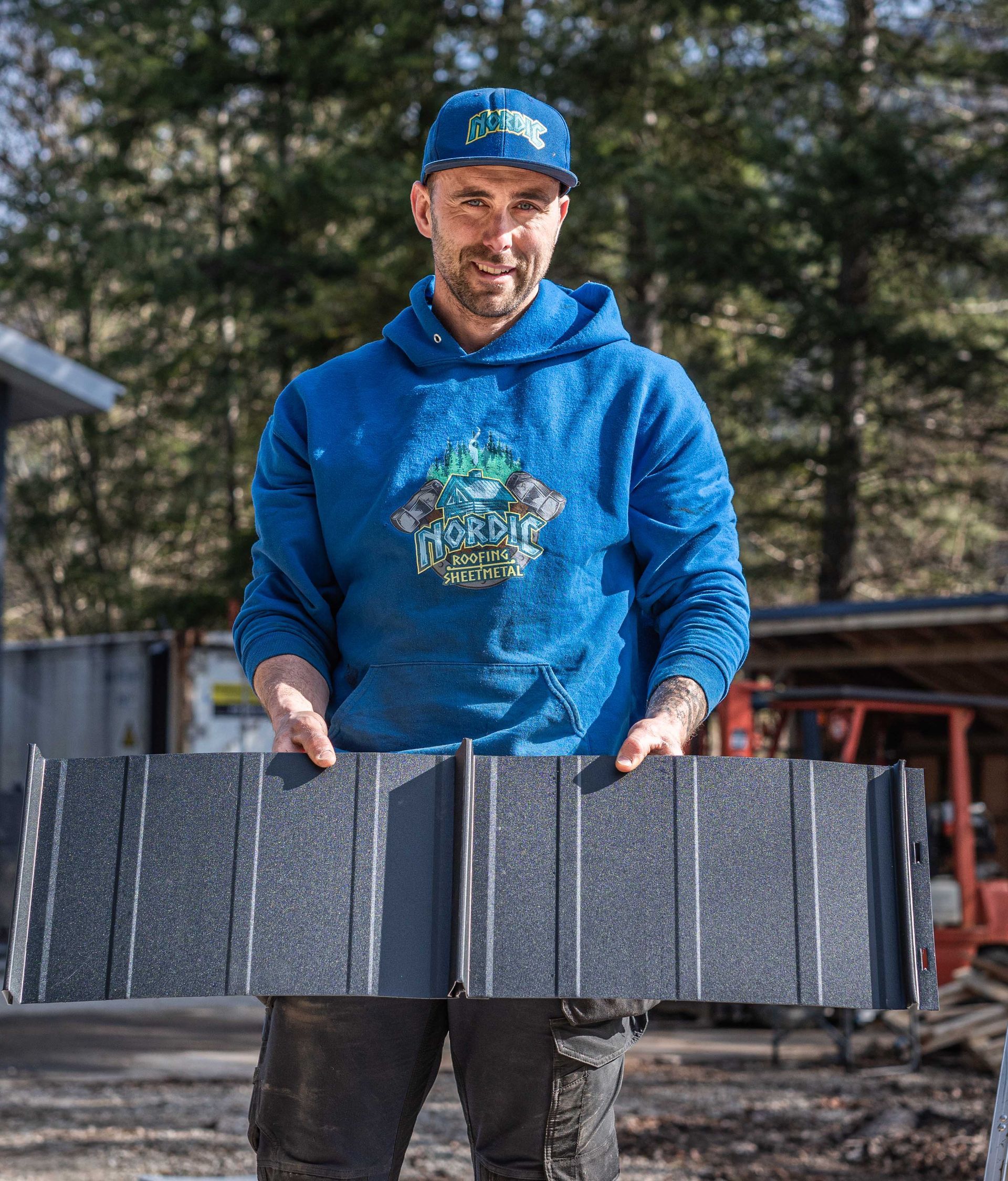 Man in blue hoodie and cap holding a large black foam panel outdoors.