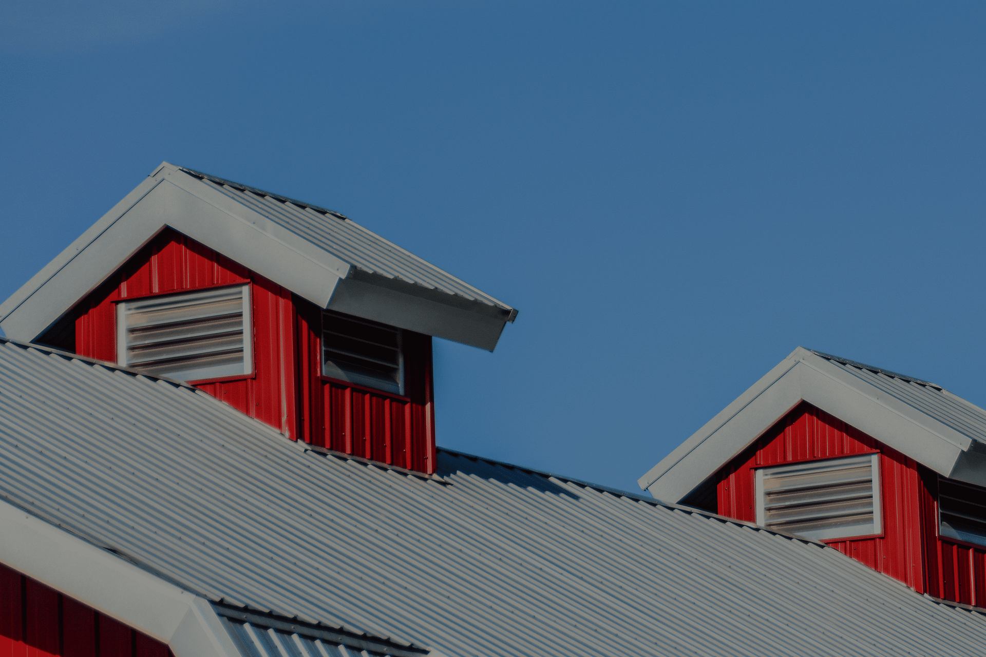 Red barn rooftops with gray metal roofs against a clear blue sky