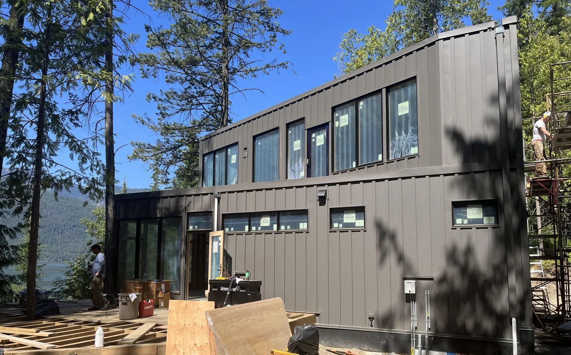 Modern gray two-story house with large windows in a wooded hillside setting