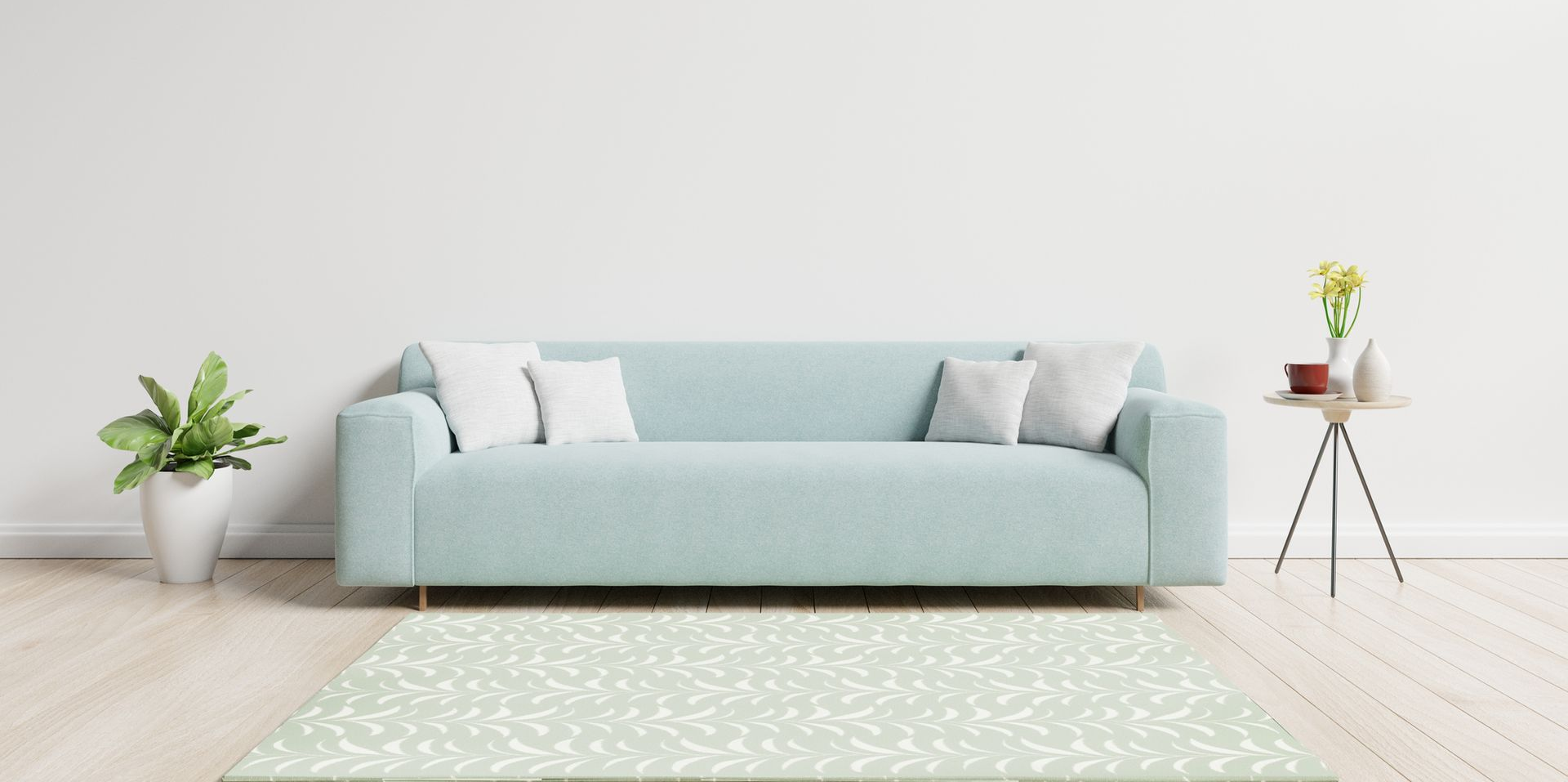 Un sofá azul claro con almohadas blancas, una alfombra y una pequeña mesa con flores en una habitación luminosa.