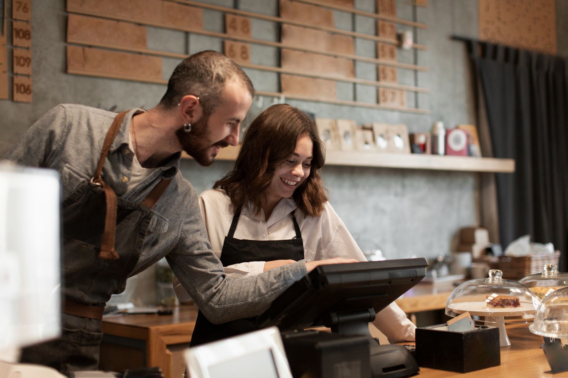 Two employees in aprons smiling while using a point-of-sale system in a coffee shop.