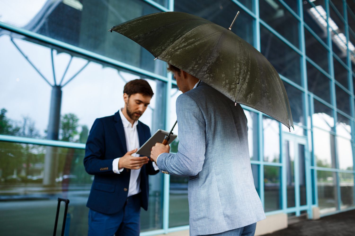 Family of three under a clear umbrella on a rainy day. Woman hugs a child; man smiles.