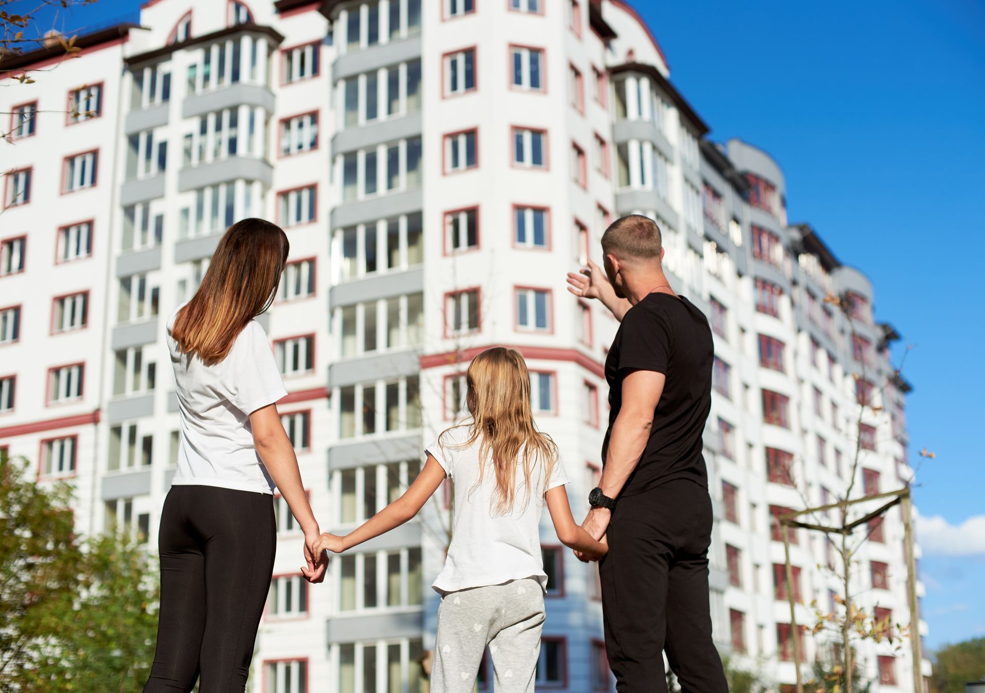 Family pointing at a tall, white apartment building with many windows under a blue sky.