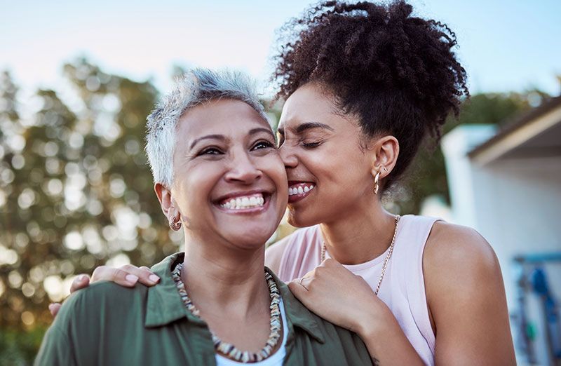 Man with beard gestures, discussing papers with a woman wearing glasses, near a plant.