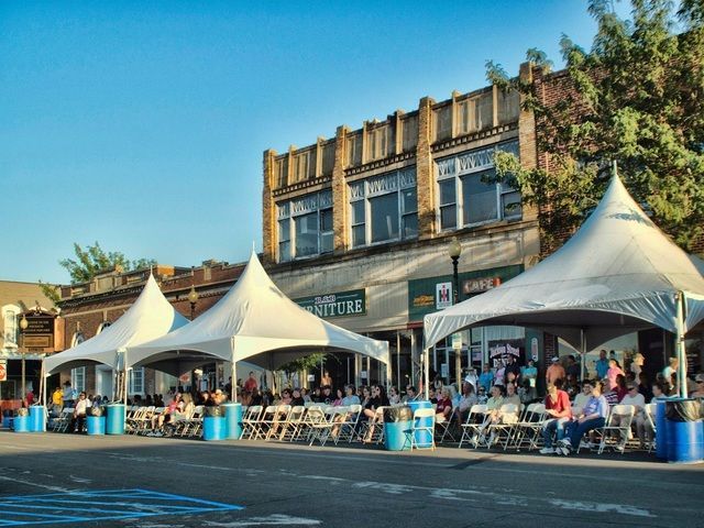 Brick building with black roof, dormers, and arched windows beneath a blue sky and tree branches.