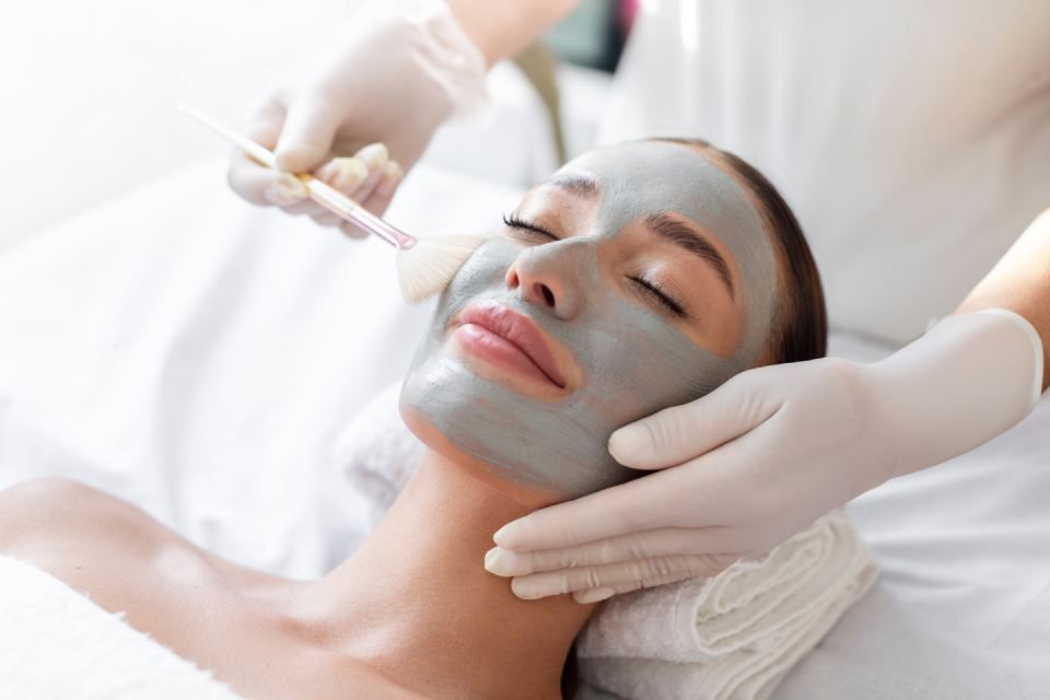 Woman receiving a facial mask in spa, with hands applying mask to face.