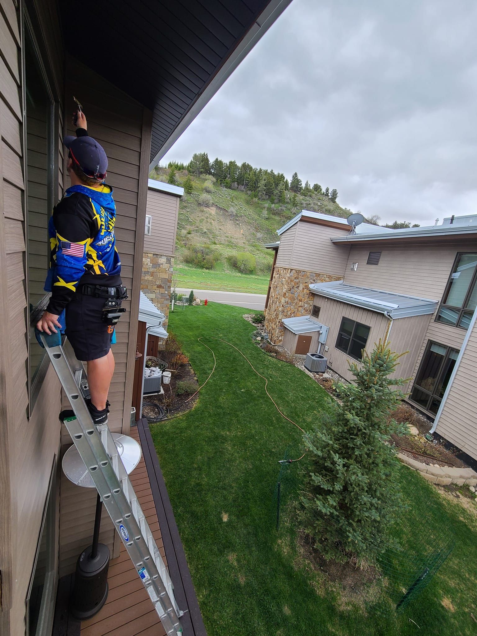 A man is standing on a ladder on the side of a building cleaning a window.
