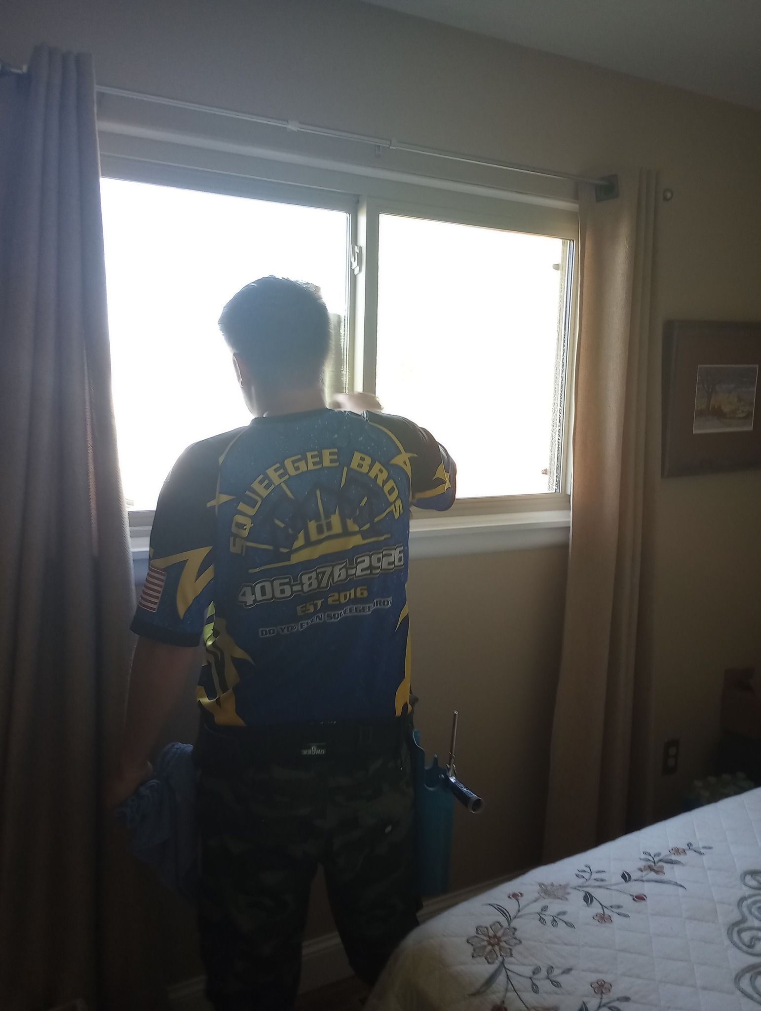 A man is standing in a bedroom looking out a window.