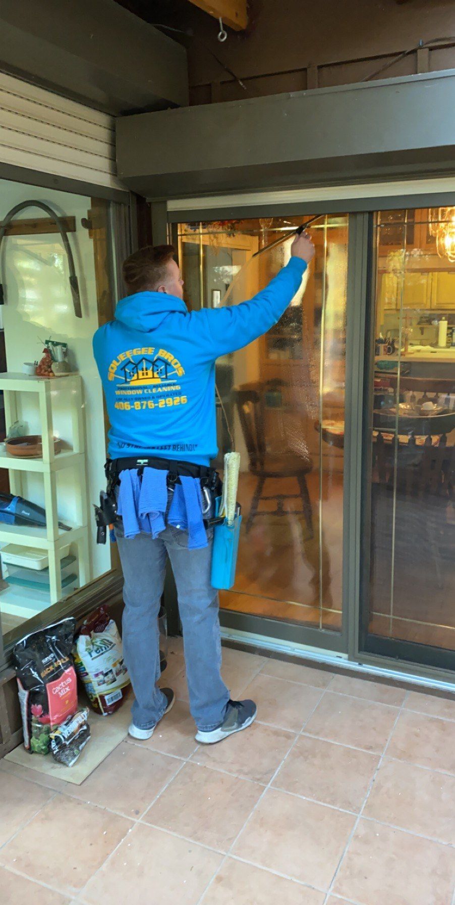 A man in a blue jacket is cleaning a sliding glass door.