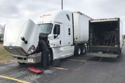A man is working on a semi truck with its hood open.