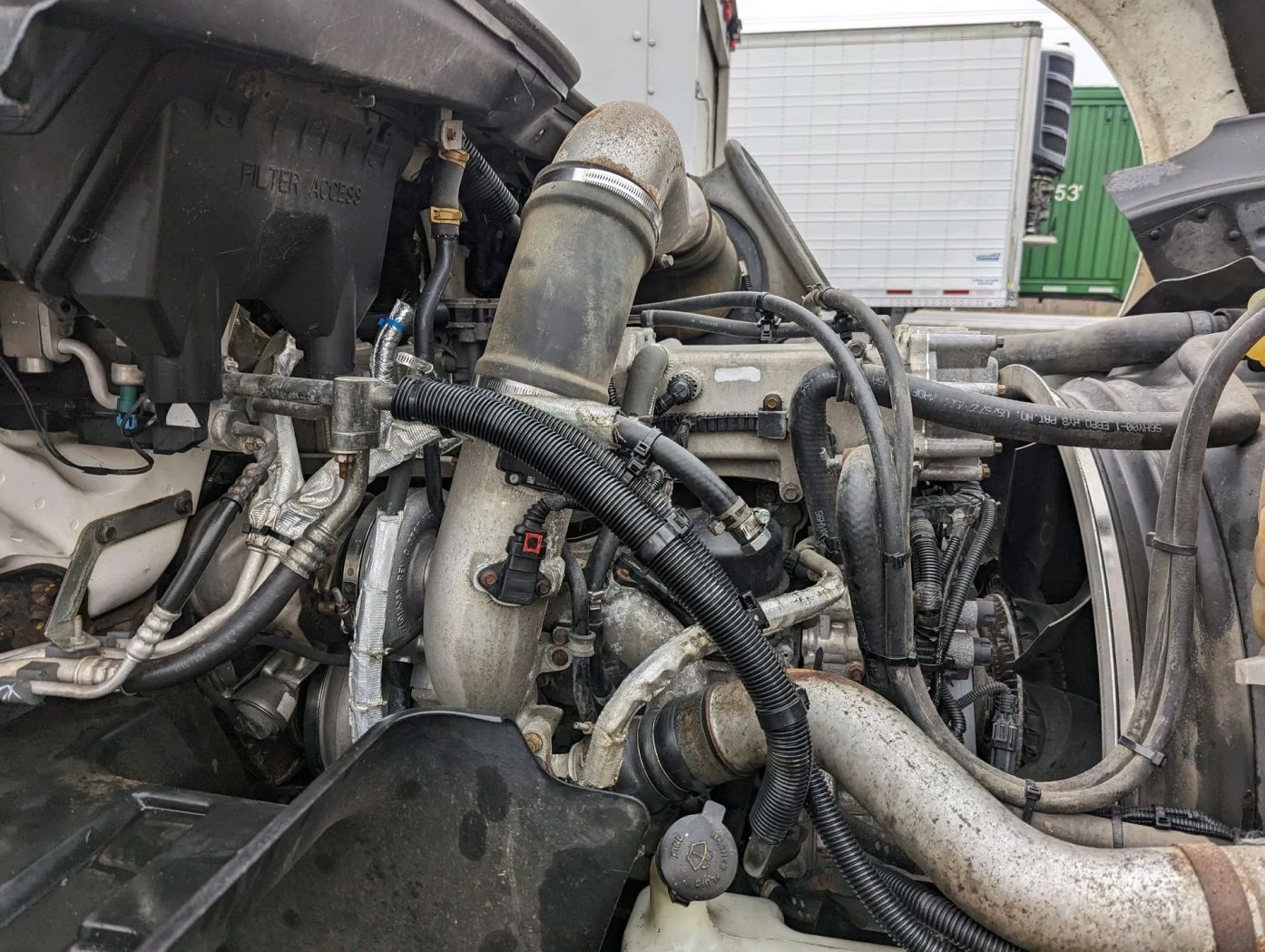 A close up of a truck engine with a green container in the background.