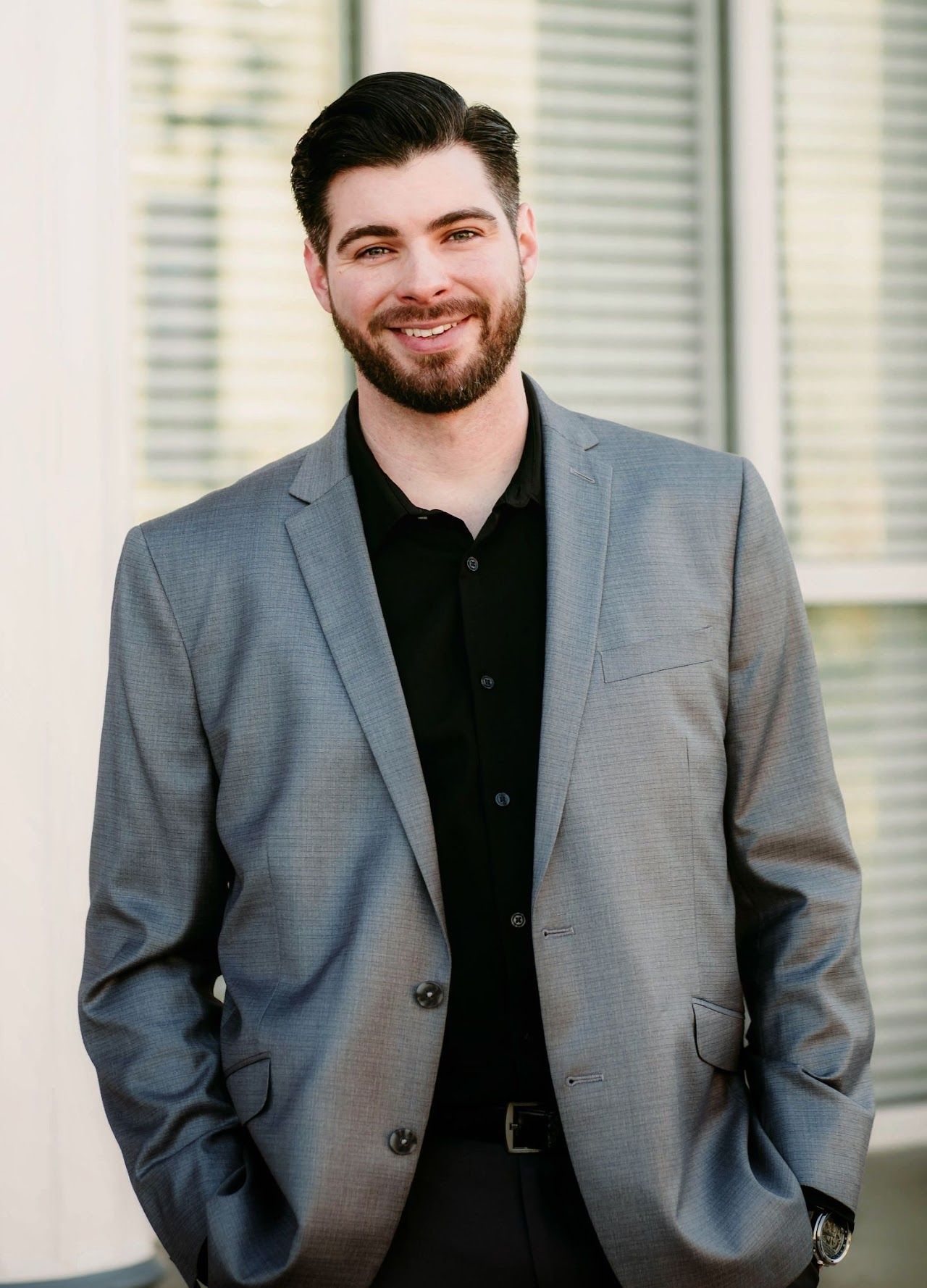 a man with a beard is wearing a grey suit and black shirt