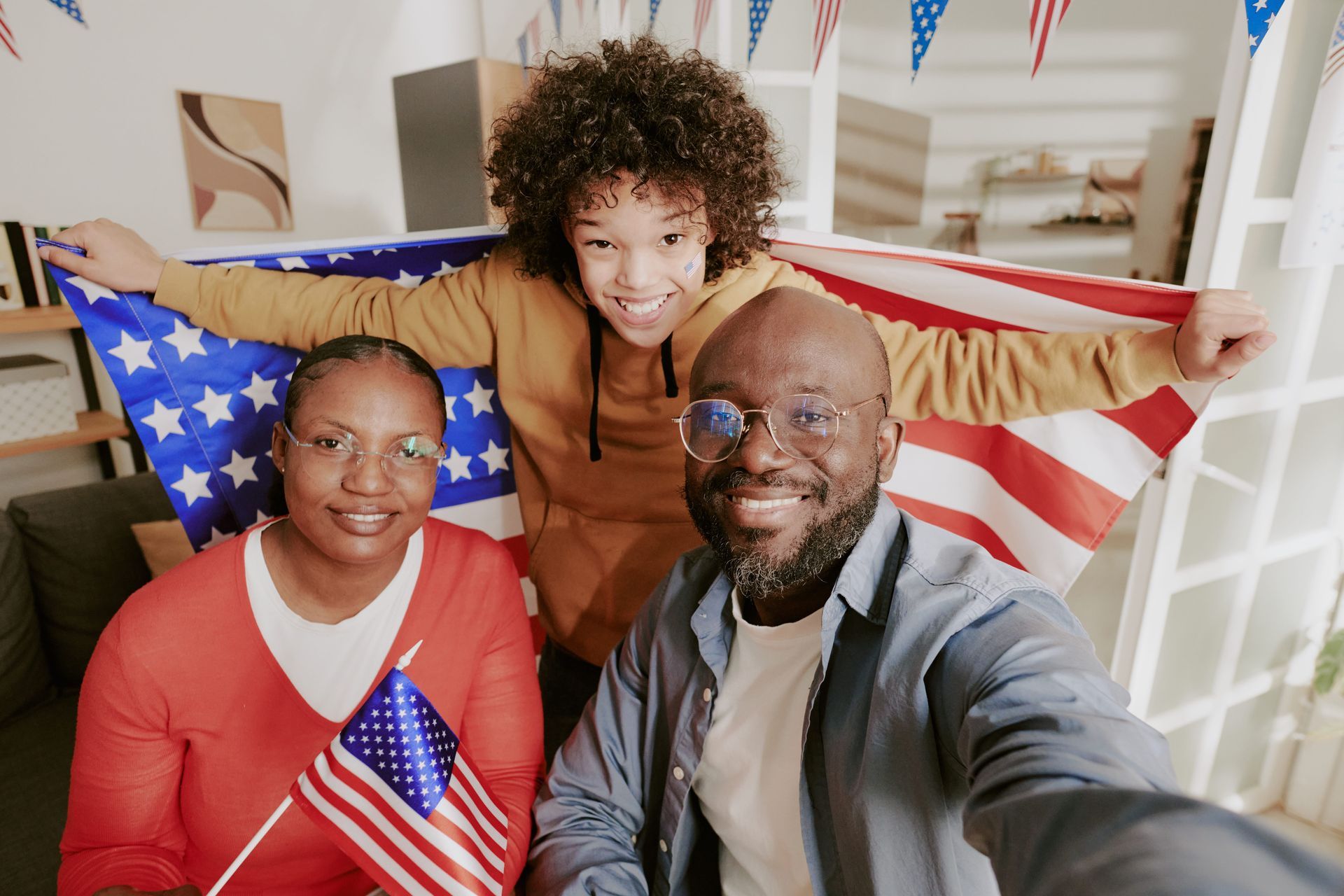 Three people smiling with an American flag draped behind them and one in front