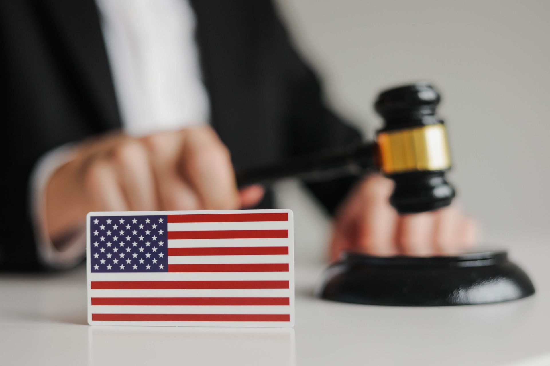 US flag in foreground with a judge’s gavel and blurred hand in the background