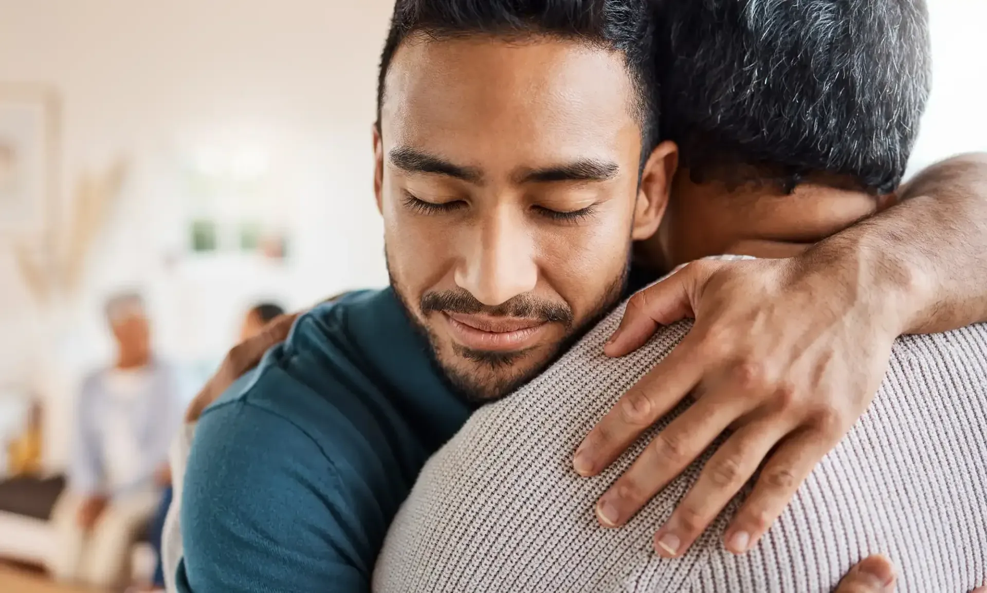 Three people standing in a room, embracing in a close, warm group hug.