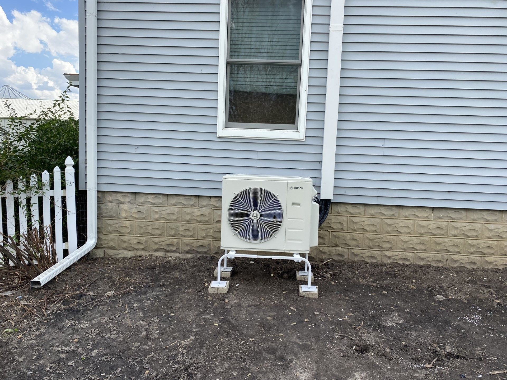 A white air conditioner is sitting on the side of a house next to a window.