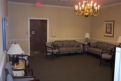 A waiting room with a couch , chairs , lamps and a chandelier.