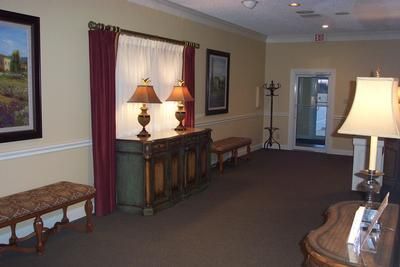 A hallway with a dresser , two lamps , a bench and a table.