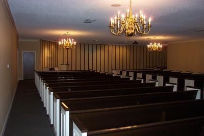 An empty church with rows of pews and a chandelier hanging from the ceiling.
