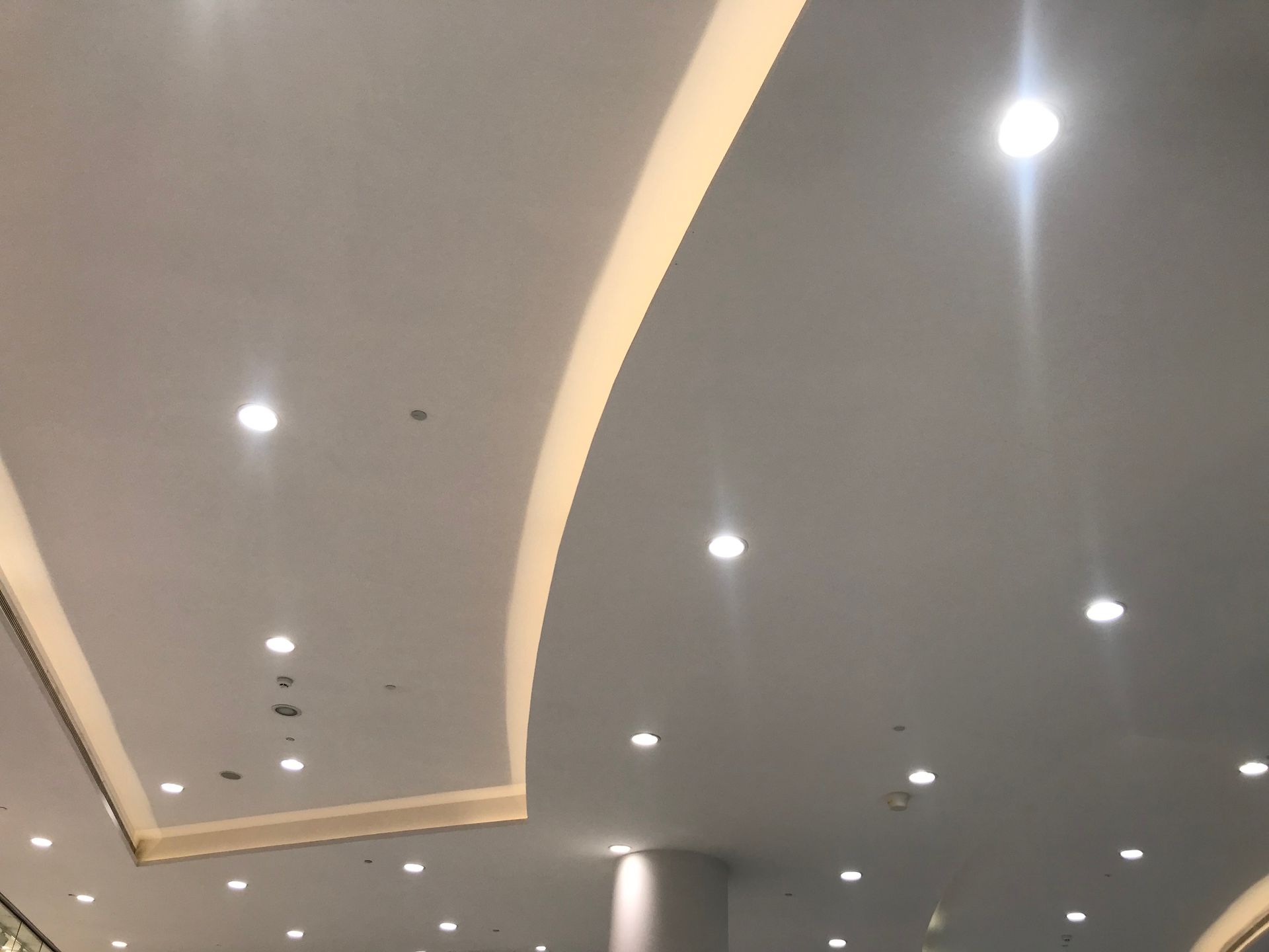 Soffitto moderno con faretti a incasso e finiture curve in un corridoio interno grigio.