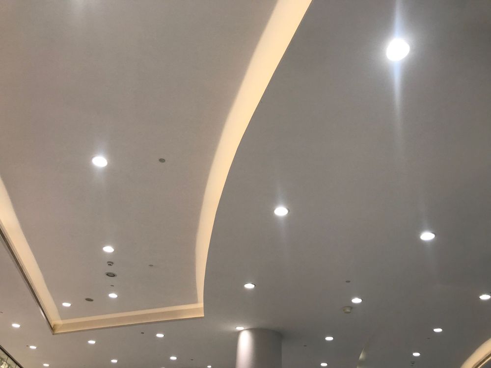 Soffitto moderno con faretti a incasso e finiture curve in un corridoio interno grigio.
