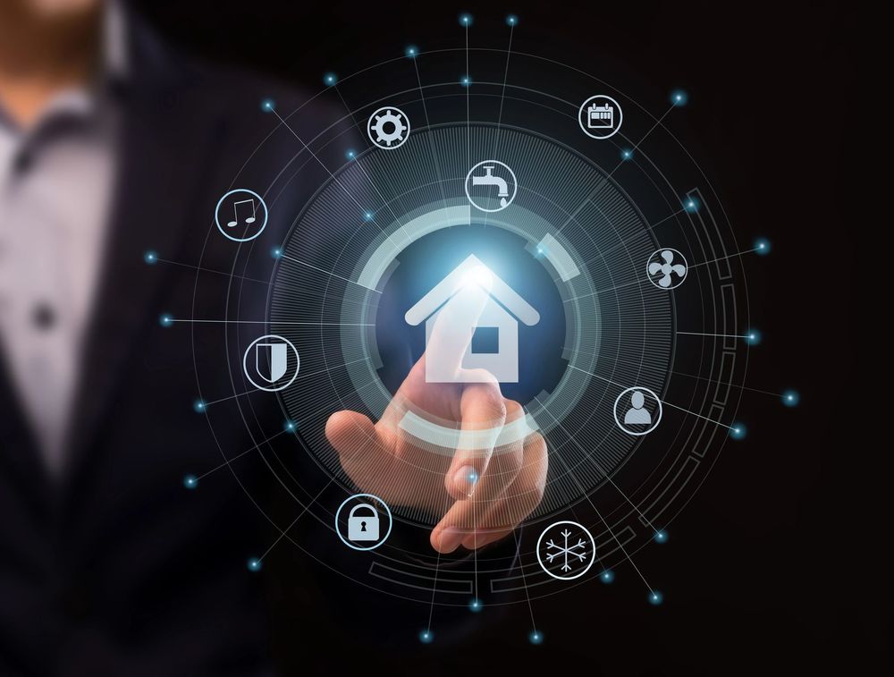Una mano preme un'icona luminosa di casa intelligente con simboli di sicurezza e automazione connessi su uno sfondo scuro.