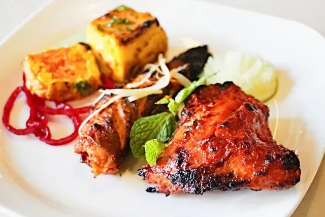 Plate of grilled Indian food: chicken, paneer, red onions, mint, lime.