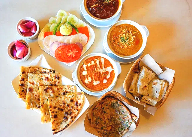 Indian spread with parathas, curries, chutneys, and sliced fruit on a white table