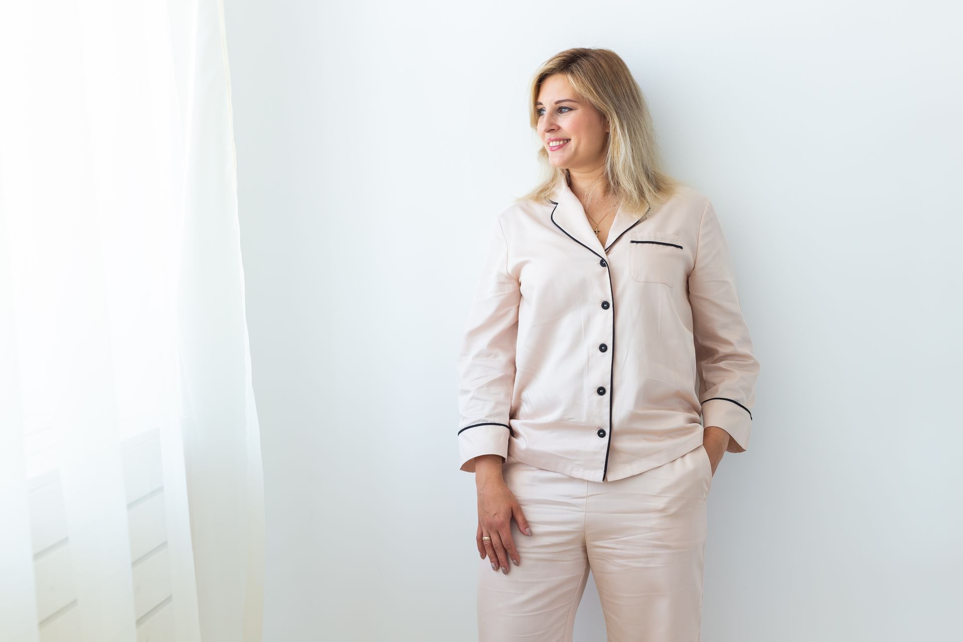 Woman in pink pajamas leans against a white wall, smiling  — Shona's Lingerie in Hermit Park, QLD