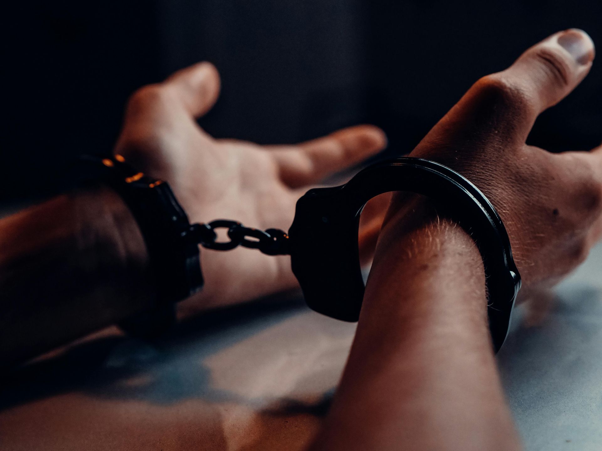 Hands in handcuffs, wrists in focus. Dark setting.