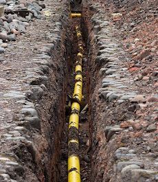 Trench showing underground yellow gas pipeline installation in rocky soil