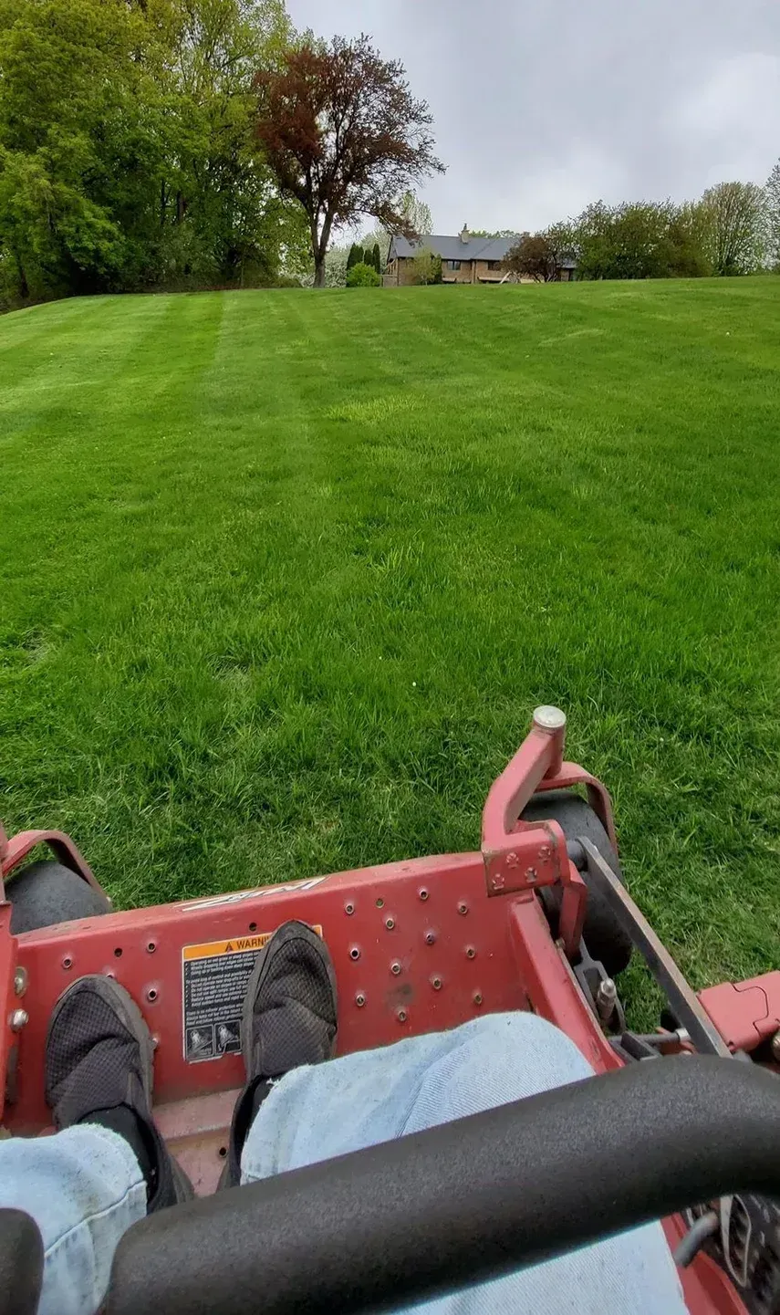 Person mowing a large, green lawn with a red zero-turn mower; overcast day.
