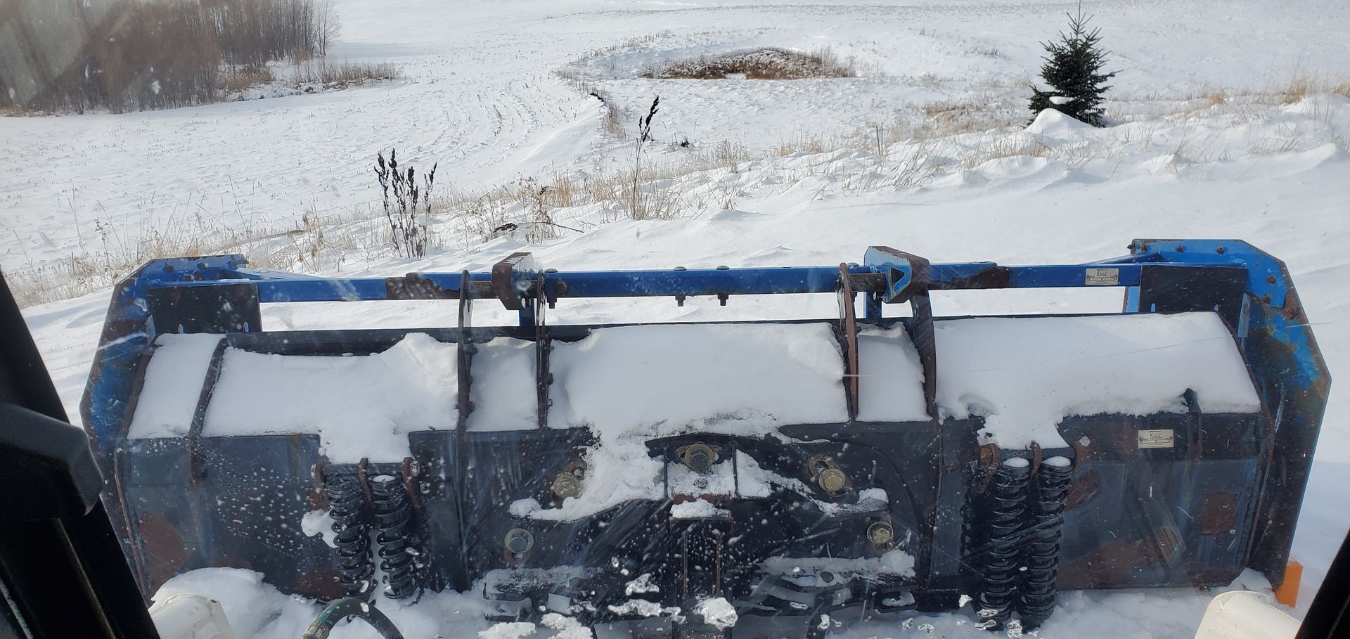 A snowplow clearing snow on a field, seen from the driver's point of view.