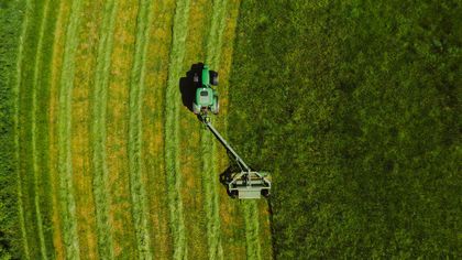 Green tractor mowing a field, creating parallel rows of cut grass.